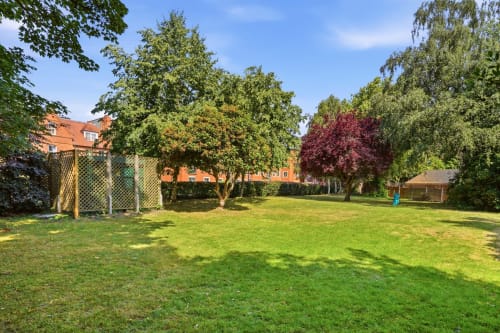 Spacious green garden at St Augustine's Place apartment in Birmingham with mature trees and brick building
