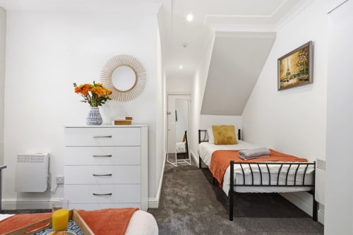 Modern apartment bedroom at 11.11 Property Estates Birmingham with orange accents, white dresser, and city view