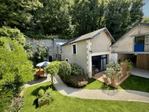 Cour de La Maison sous les Vignes, gîte avec bâtiments blancs modernes, jardins luxuriants et pelouse verte en France