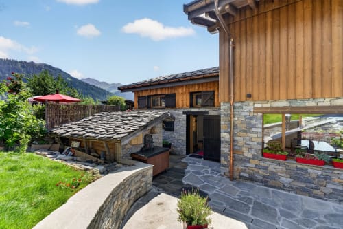 Chalet de luxe L'Alp'In aux façades pierre et bois, vue montagne, terrasse avec parasol rouge à La Plagne Tarentaise