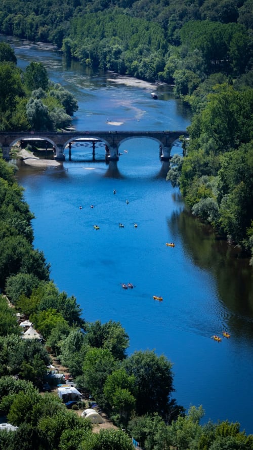 Vue pittoresque de la rivière avec pont en pierre et kayakistes près du glamping Home Sweet Lodge en Aquitaine