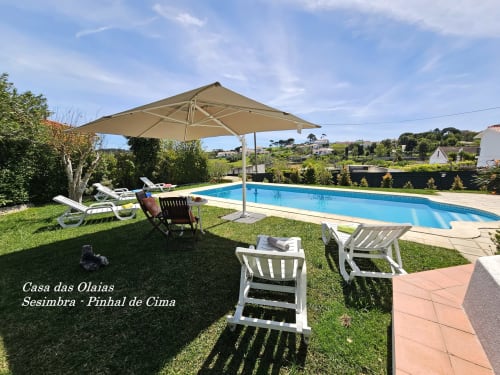Casa das Olaias villa in Sesimbra with private pool, lounge chairs, beige umbrella, and lush green grounds overlooking the