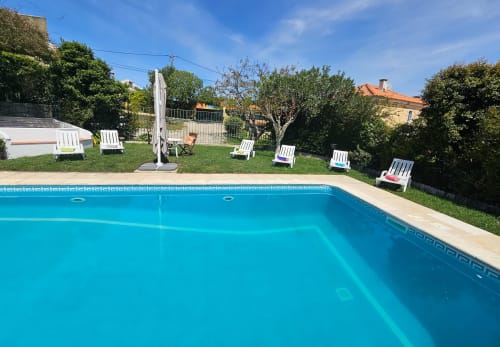 Crystal-blue private pool at Casa Oleias villa in Sesimbra with white loungers, manicured garden, and scenic countryside