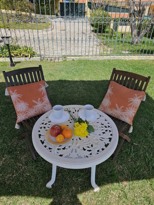 Two black wooden chairs with coral cushions beside a round white table with fresh fruit and flowers in the garden at Sesimbra