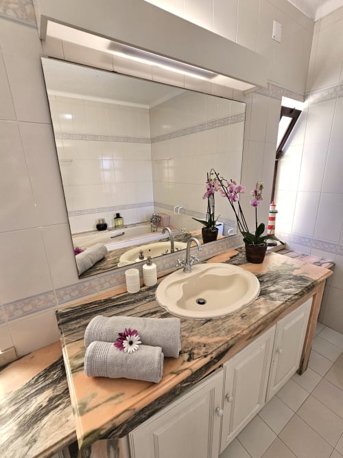 Elegant bathroom vanity with marble countertop, round sink, and large mirror at Casa Oleias villa in Sesimbra