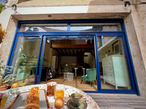 Portes-fenêtres à cadre bleu ouvrant sur l'espace de vie moderne de La Maison sous les Vignes, avec table de petit-déjeuner