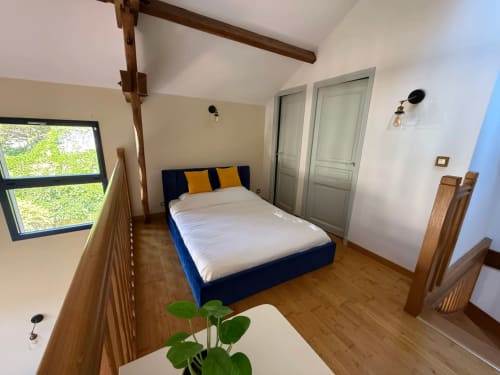 Chambre spacieuse à La Maison sous les Vignes avec lit bleu, poutres en bois et vue sur les vignobles depuis la fenêtre