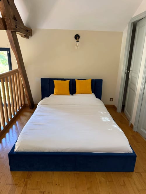Chambre moderne à La Maison sous les Vignes avec lit capitonné bleu marine, draps blancs, oreillers jaunes, parquet