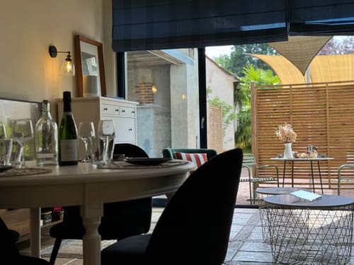 Élégante salle à manger de la Maison sous les Vignes avec service de vin, ouvrant sur une terrasse de jardin en bois en France