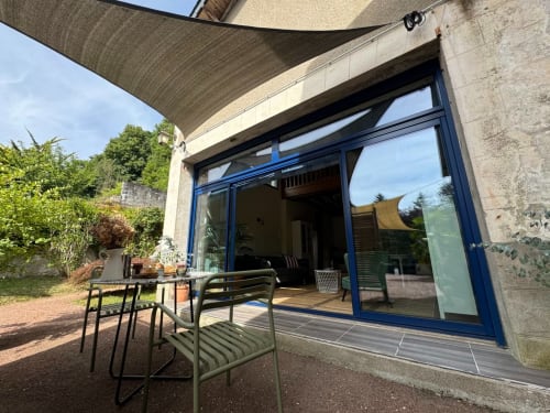 Terrasse moderne avec portes vitrées bleues à La Maison sous les Vignes, ombragée par une voile d'ombrage