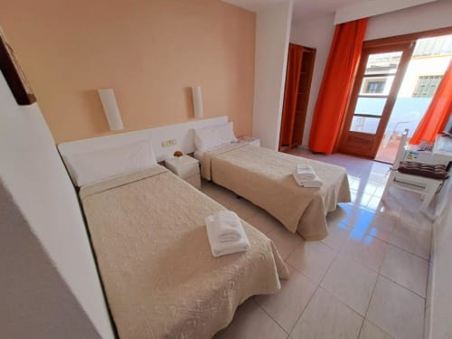 Camera luminosa a La Casita di Fuerte con due letti singoli, pareti in terracotta e tende rosse affacciata su Caleta de