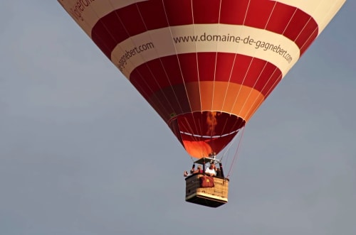 Montgolfière aux rayures rouges et crème survolant les vignobles de France près de La Maison sous les Vignes