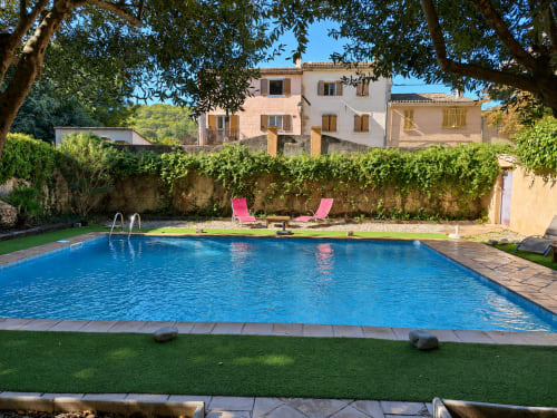 Piscine bleu cristal de l'Auberge du Parc à Correns avec transats rose, pelouse impeccable et oliviers