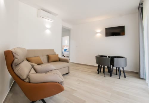 Modern apartment living room in Amadora, Lisboa with beige sofa, orange accent chair, dining table, TV, and light wood