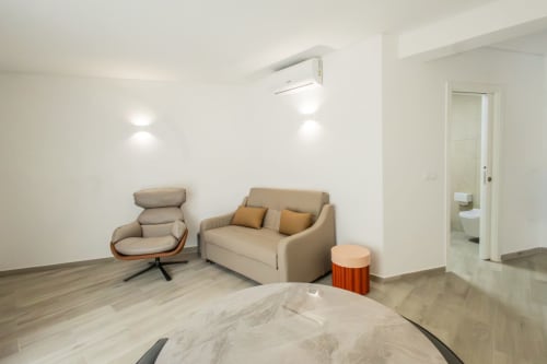 Modern J Home apartment living room in Amadora with beige sofa, armchair, wooden floors, and ensuite bathroom
