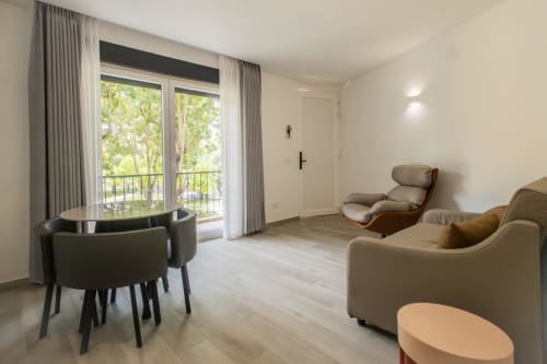 Modern T2 apartment living room at J Home Amadora with seating, dining table, and balcony overlooking green park area in