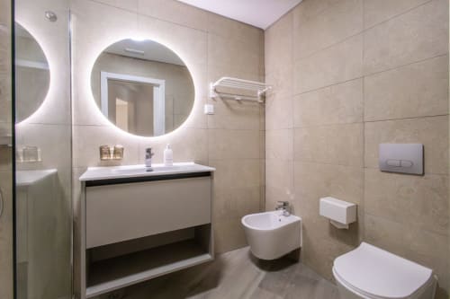 Modern bathroom at J Home Amadora with illuminated mirror, sink, bidet, toilet, and neutral tile walls