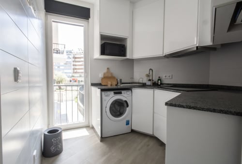 Modern kitchen in J Home Amadora apartment with white cabinets, washing machine, black granite counters, and balcony