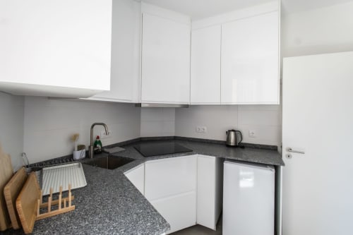 Modern kitchen in J Home Amadora apartment with white cabinets, dark granite countertops, and stainless steel appliances in