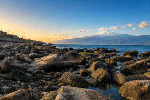 Costa rocciosa con l'Etna innevato al tramonto, Reggio Calabria, Italia