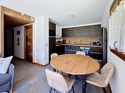 Cuisine ouverte et salle à manger de l'appartement La Tanière du Tétras à Montgenèvre, avec table ronde en bois et placards noirs