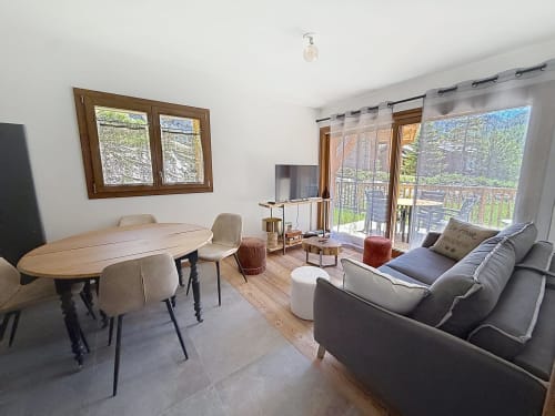 Salon moderne avec table à manger, canapé gris, télévision et vue sur les montagnes par les portes vitrées aux Tanières de