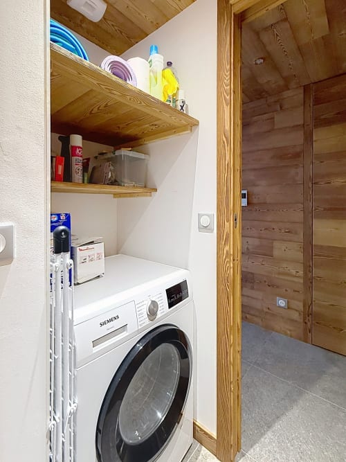 Buanderie avec lave-linge Siemens, étagères en bois avec produits d'entretien, porte encadrée en bois aux Tanières de