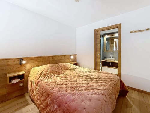 Chambre avec tête de lit en bois et literie dorée aux Tanières de Montgenèvre, salle de bain attenante visible par la porte