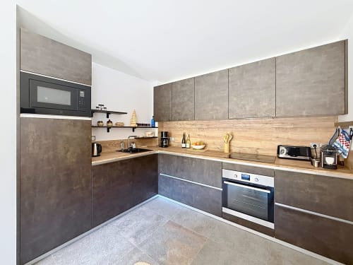 Cuisine moderne avec armoires en brun, comptoirs en bois et électroménagers en acier inoxydable à l'appartement La Tanière du Tétras