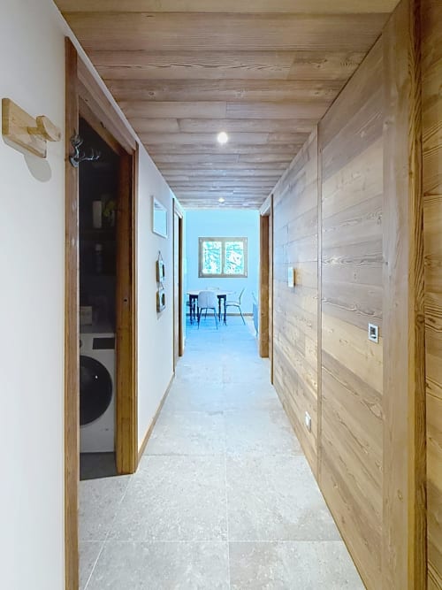 Couloir contemporain des Tanières de Montgenèvre avec poutres en bois, carrelage en pierre et accès aux espaces de vie