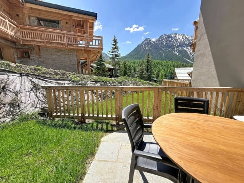 Terrasse panoramique des Tanières de Montgenèvre avec table à dîner, balustrade en bois et Alpes enneigées en arrière-plan