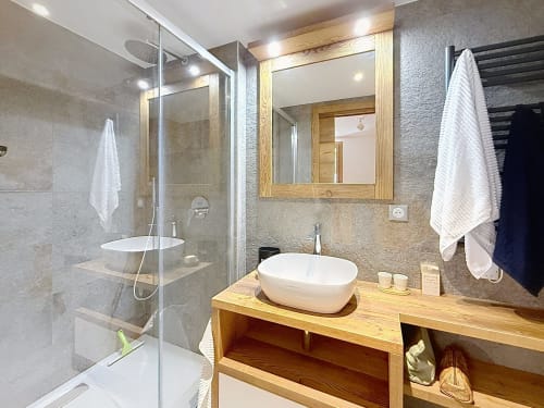 Salle de bain moderne aux Tanières de Montgenèvre avec vasque en bois, lavabo ovale, miroir encadré et douche vitrée