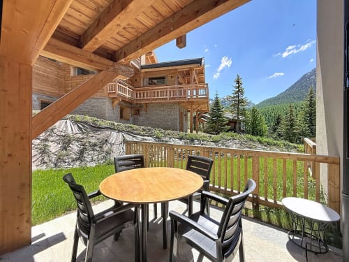 Terrasse ensoleillée aux Tanières de Montgenèvre avec table de repas, chaises, garde-corps bois et vues sur la vallée alpine