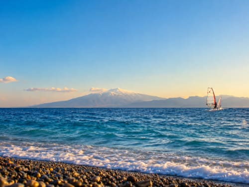 Windsurfista sul mare turchese con l'Etna innevato, spiaggia di ciottoli del B&B Pellicano, Reggio Calabria