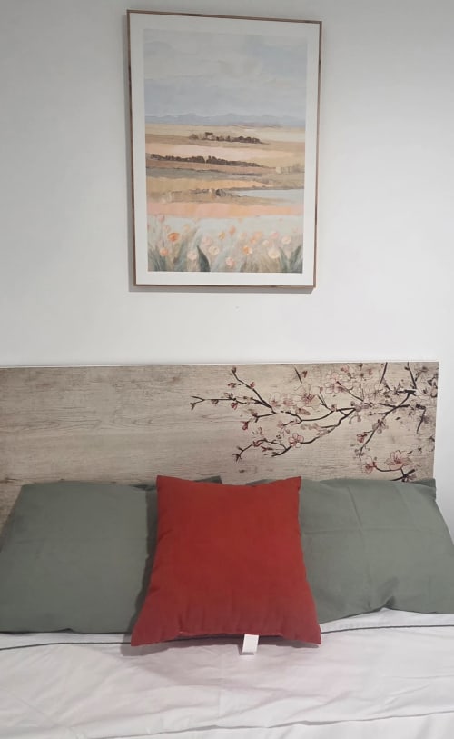 Acogedora habitación del hostal Suki House con obra de arte paisajística enmarcada, cabecero de madera con detalles florales y almohada roja sobre fondo sage