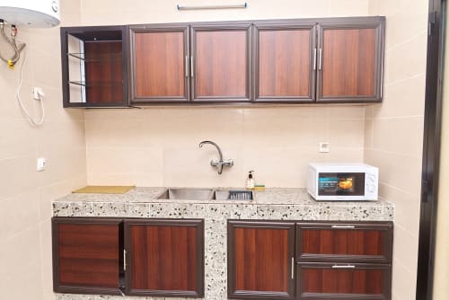 Kitchenette moderne à l'Hôtel Yakro avec armoires en bois, plan de travail en granit, évier, micro-ondes et rangements muraux
