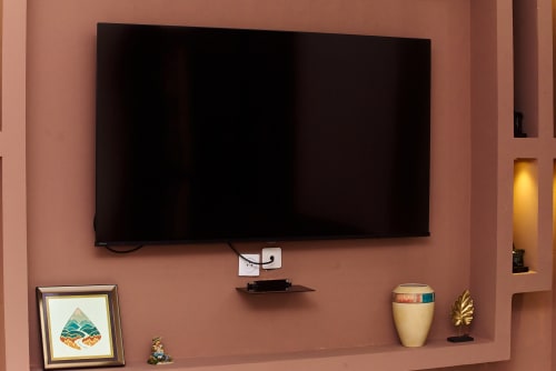 Téléviseur écran plat fixé à un mur en terre cuite avec étagère flottante et objets de décoration à l'Hôtel Yakro, Yamoussoukro