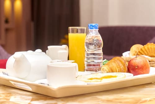 Plateau de petit-déjeuner à l'Hôtel Yakro avec jus d'orange, croissant, pomme, bouteille d'eau et vaisselle blanche sur surface en bois.