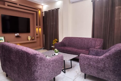 Spacieux salon de l'Hôtel Yakro avec sièges violets, télévision écran plat, mobilier moderne et décoration élégante à Yamoussoukro