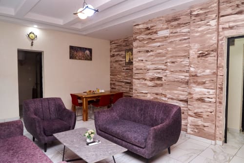 Salon moderne de l'appartement Hôtel Yakro avec canapés violets, mur d'accent en bois et coin repas à Yamoussoukro