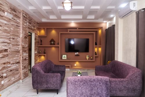 Salon moderne de l'Hôtel Yakro avec fauteuils violets, téléviseur écran plat sur mur terracotta et mur d'accent bois