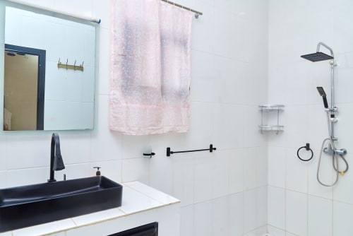 Salle de bains moderne de l'Hôtel Yakro avec lavabo noir, carrelage blanc, douche pluie et serviette rose à Yamoussoukro