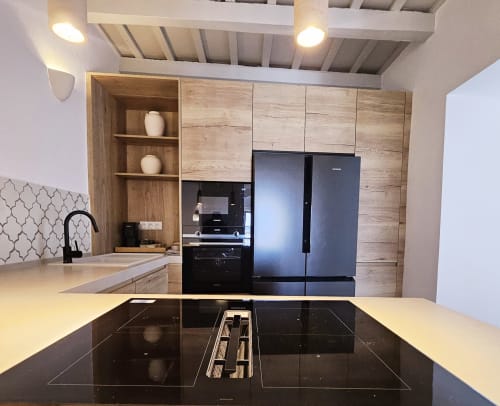 Cocina moderna con placa de inducción negra, electrodomésticos de acero inoxidable y muebles de madera en Casa De La Cruz Vejer