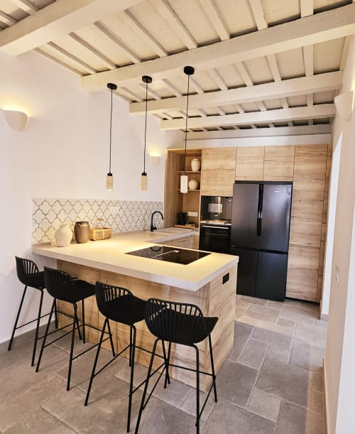 Cocina moderna con gabinetes de madera, encimeras blancas, electrodomésticos negros e isla con asientos en Casa De La Cruz Vejer