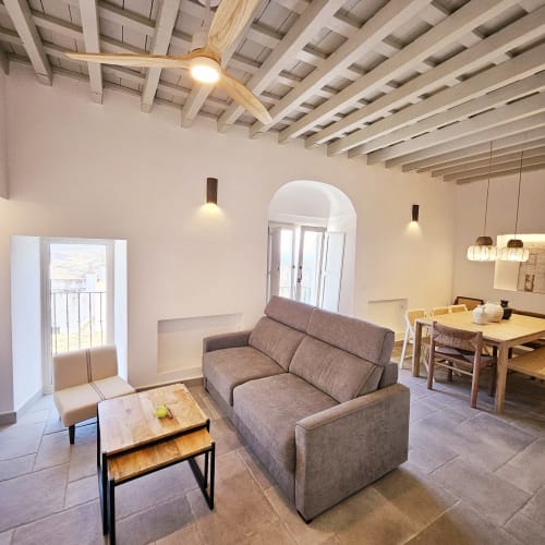 Moderna sala de estar con sofá gris, mesa de comedor de madera y techo de vigas expuestas en apartamento Casa De La Cruz Vejer