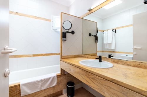 Baño moderno del Smart Hotel Cabo Sur en Mojácar con mueble de madera, lavamanos blanco y ducha a ras de suelo con cabina de cristal.