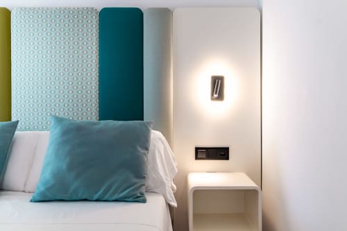 Habitación moderna del Smart Hotel Cabo Sur con almohada azul turquesa, panel de cabecera geométrico, aplique de pared y rincón mesita de noche