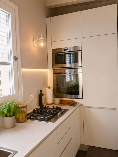 Cucina moderna con mobili color crema, elettrodomestici in acciaio inossidabile, piano cottura a gas e finestra presso la Guest House B&B Pellicano