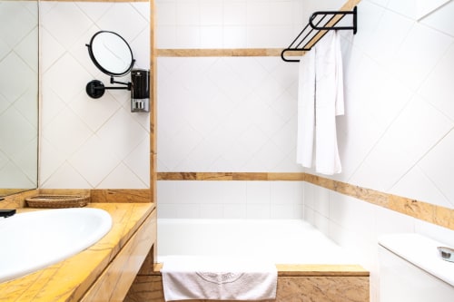 Baño moderno del Smart Hotel Cabo Sur en Mojácar con azulejos blancos, tocador de madera, espejo mural y bañera con toallero.