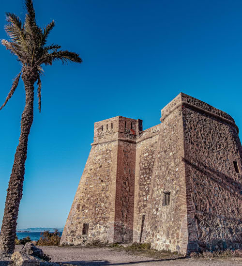 Torre de piedra histórica con palmera vista al mar Mediterráneo, Mojácar España